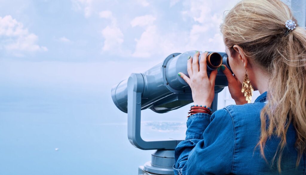 Blonde woman using a tower viewer to observe the ocean on a clear day.